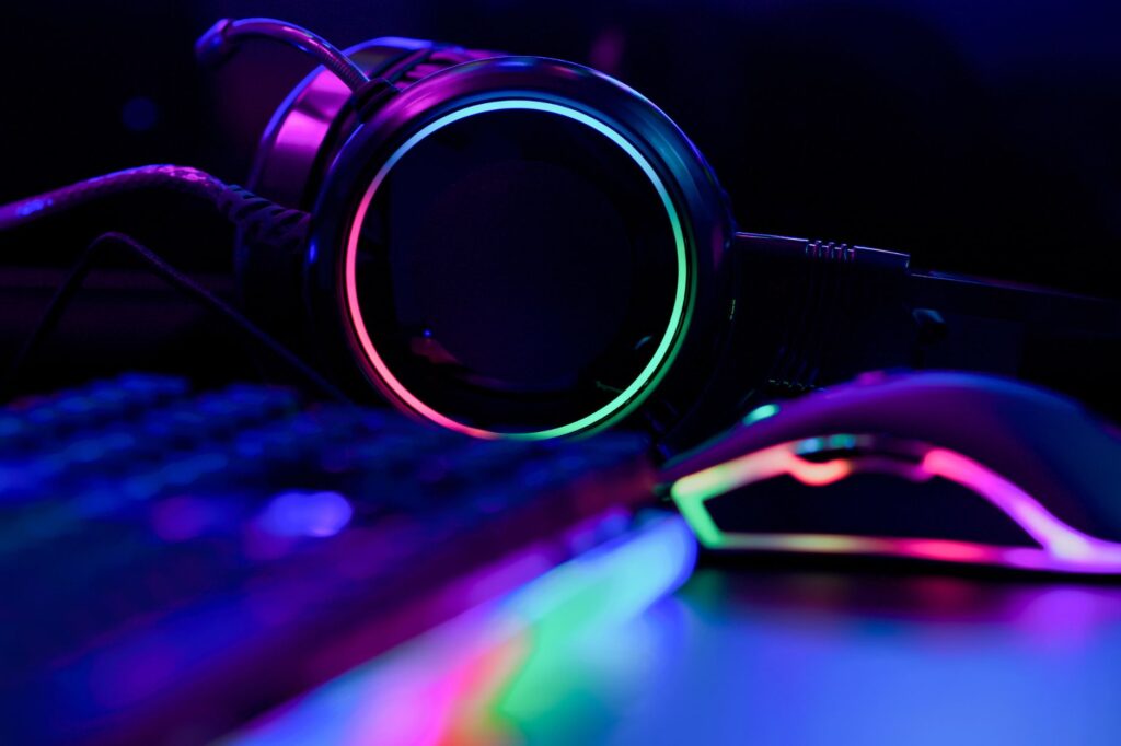 In a dimly lit room, the RGB glow of gaming headphones, keyboard, and mouse creates an immersive atmosphere akin to a cyber resilience strategy's defense portal.